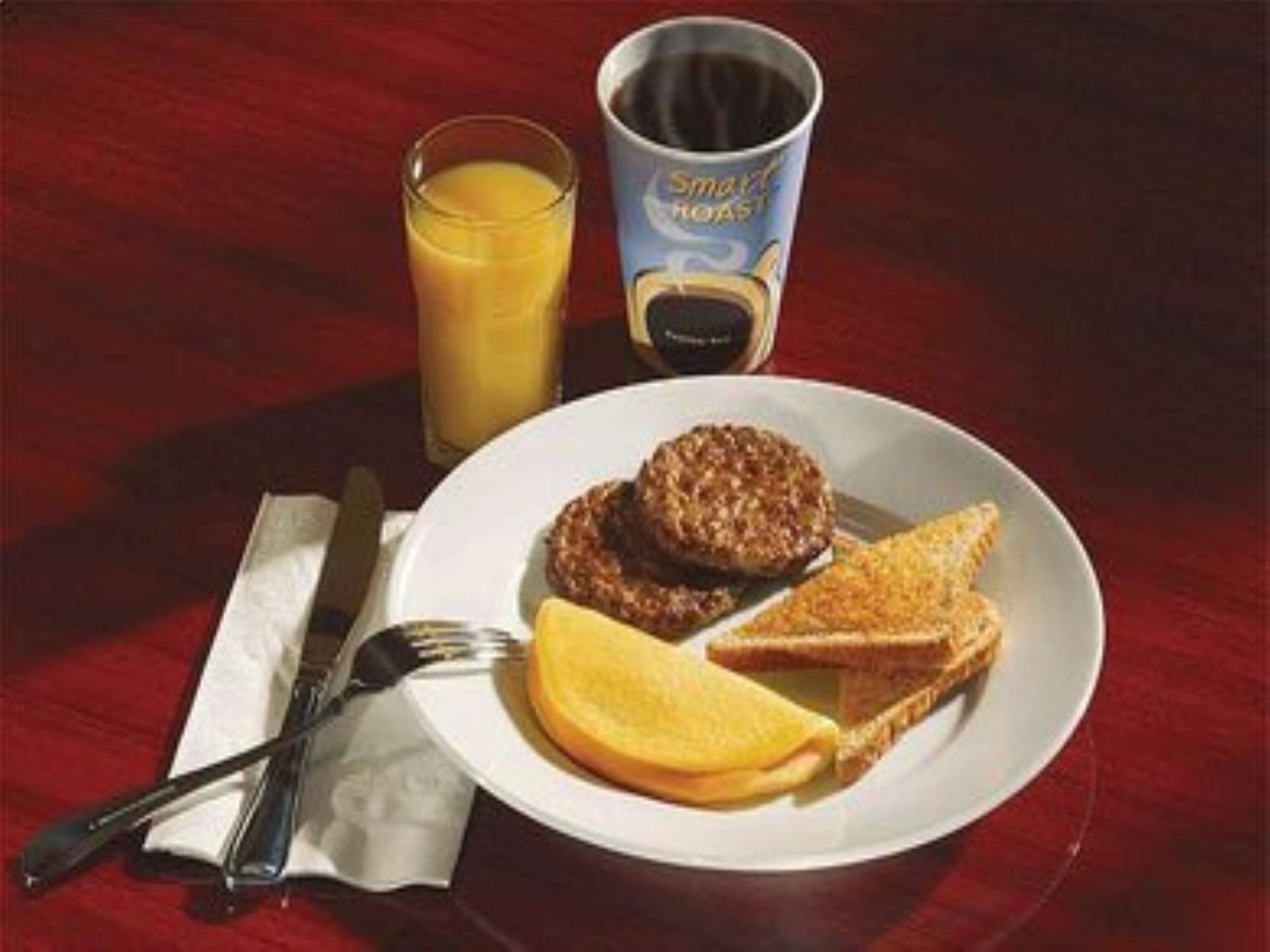 A breakfast plate with scrambled eggs, a sausage patty, toast, and a glass of orange juice.