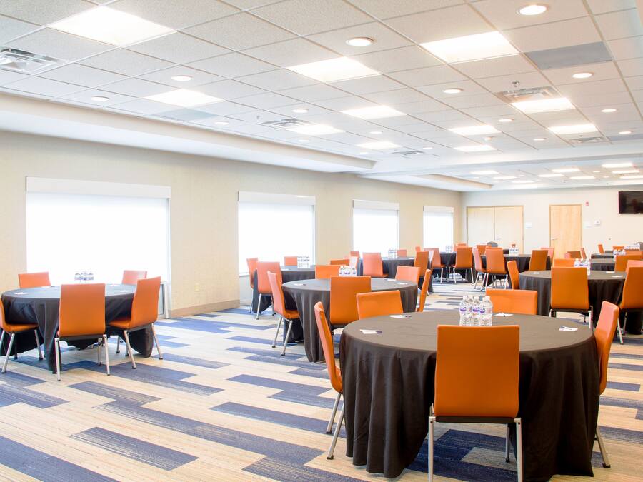 A conference room with multiple tables and chairs, arranged in rows, with a carpeted floor and a ceiling with recessed lighting.