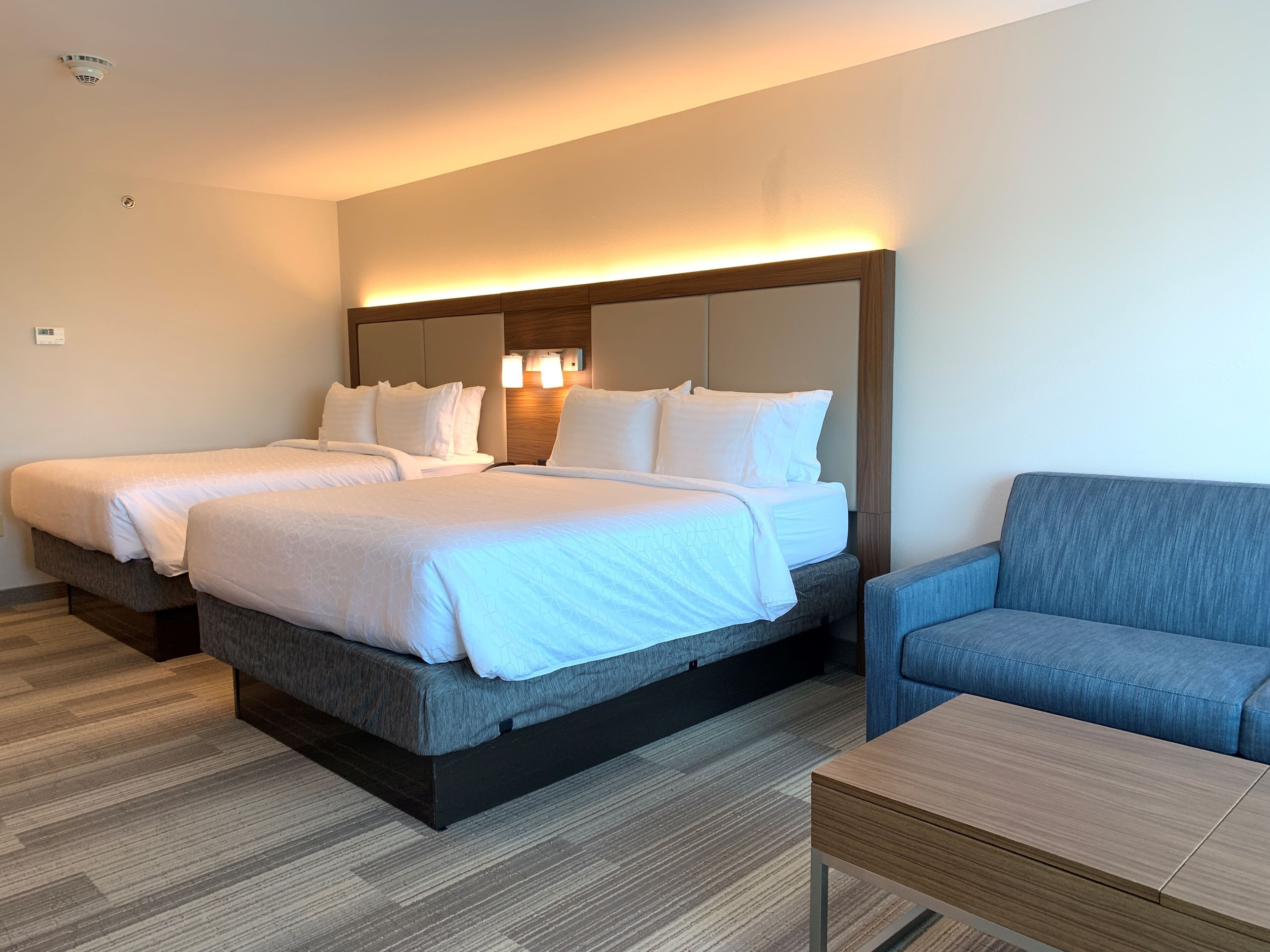 Quarto de hotel com duas camas, um sofá e uma pequena mesa.