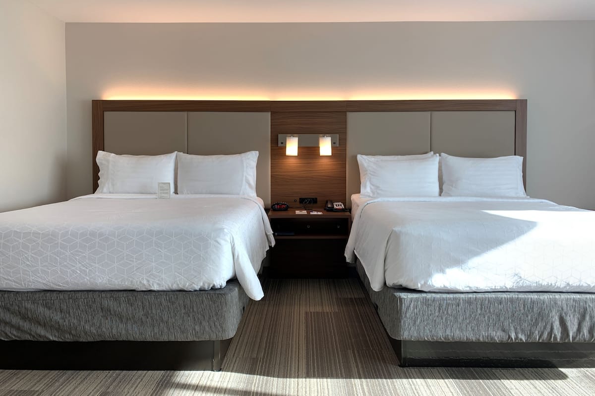 A hotel room with two beds, a nightstand, and a wall-mounted light fixture.