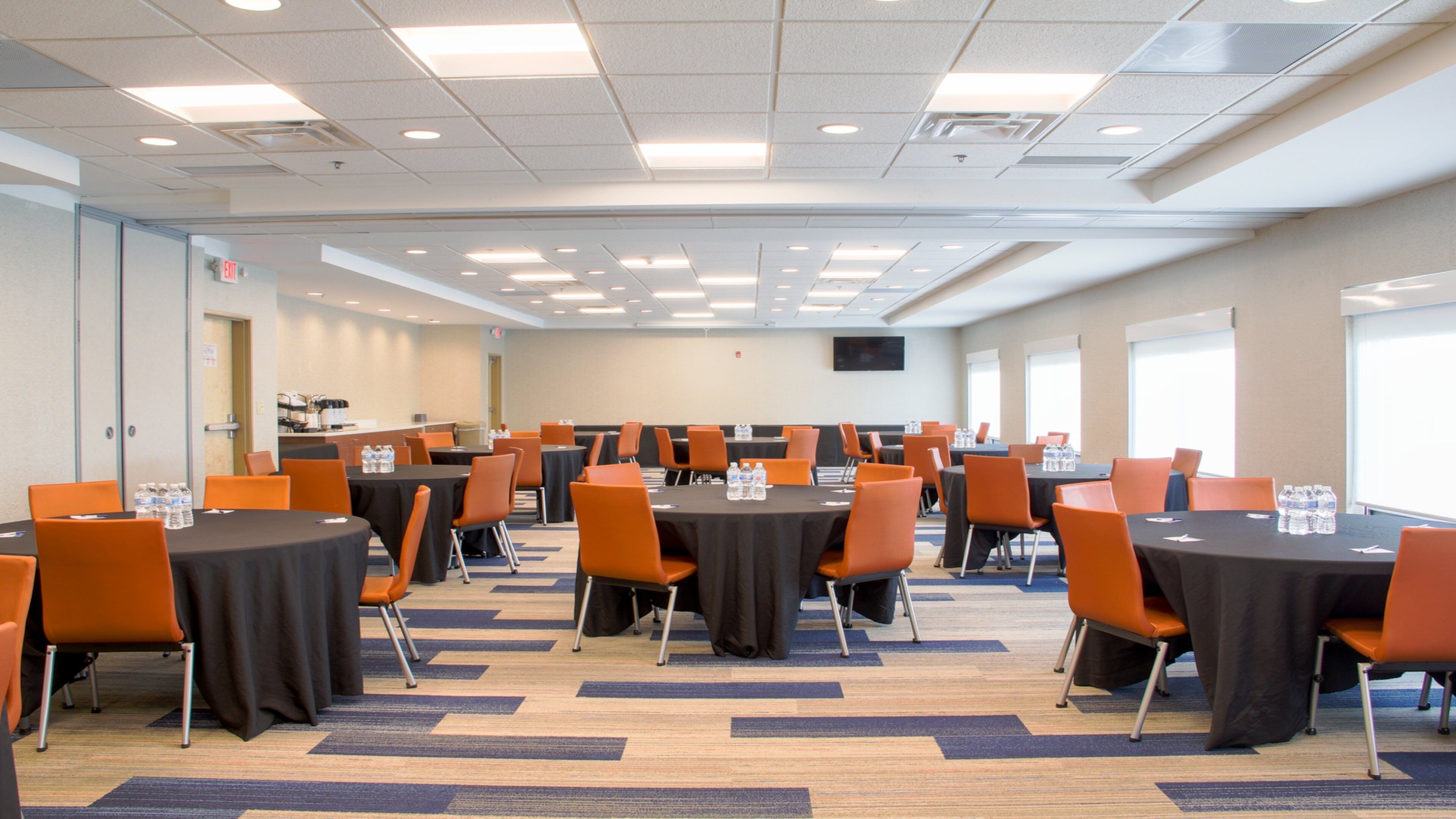 A conference room with multiple tables and chairs, equipped with water bottles, and a carpeted floor.