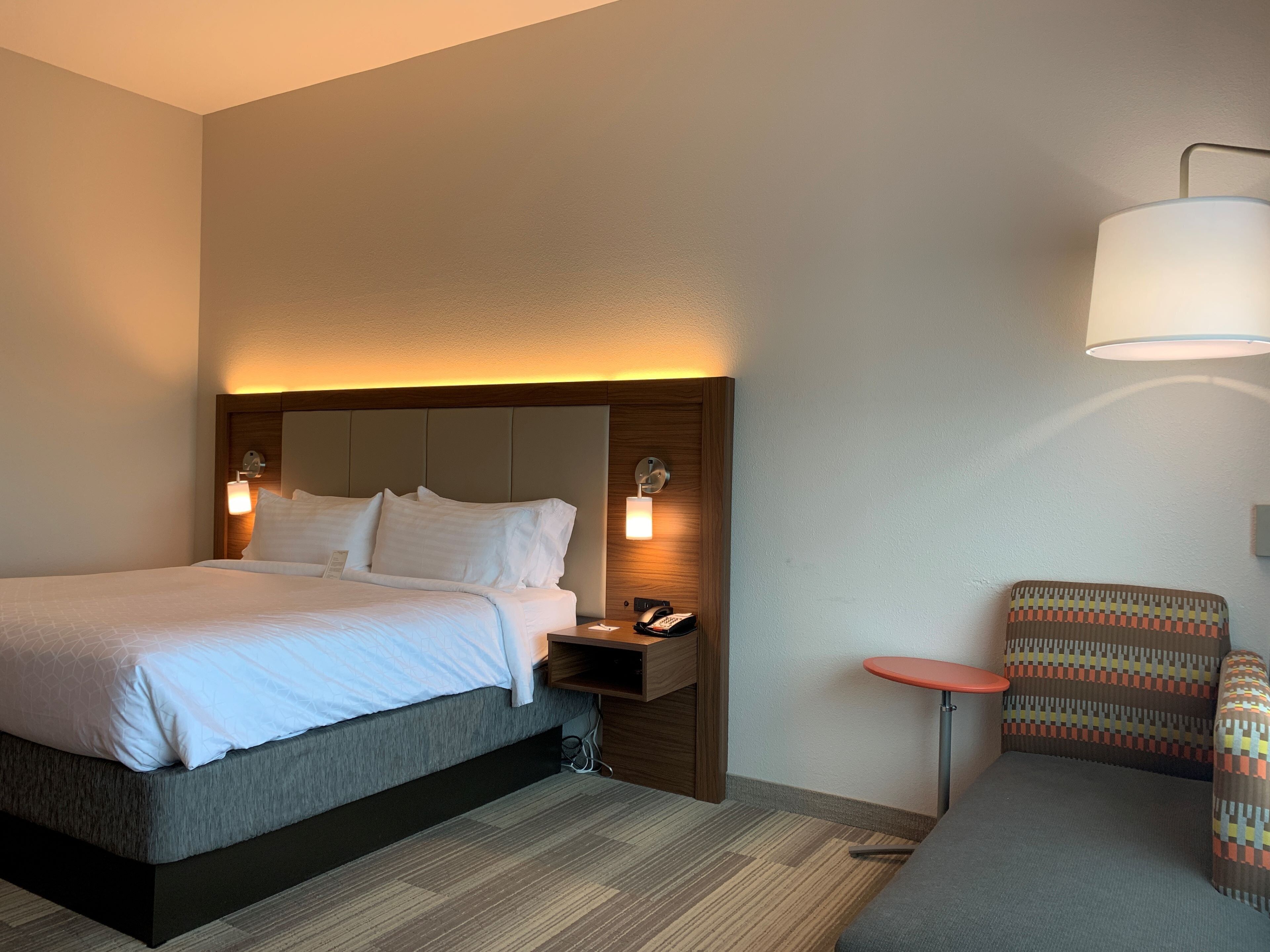 Une chambre d’hôtel comprenant un lit, une table de chevet, une lampe et un petit coin salon.