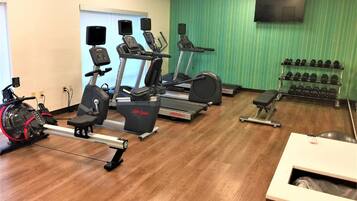 A gym with cardio machines, dumbbells, and a TV on the wall.