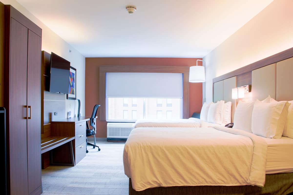 A hotel room with a large bed, a desk with a chair, a television, and a window with blinds.