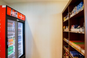Un distributeur automatique orné d’une enseigne Coca-Cola et dont l’étagère est remplie de divers produits.