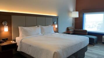 A hotel room with a large bed, bedside tables, a lamp, and a view of the city through a window.