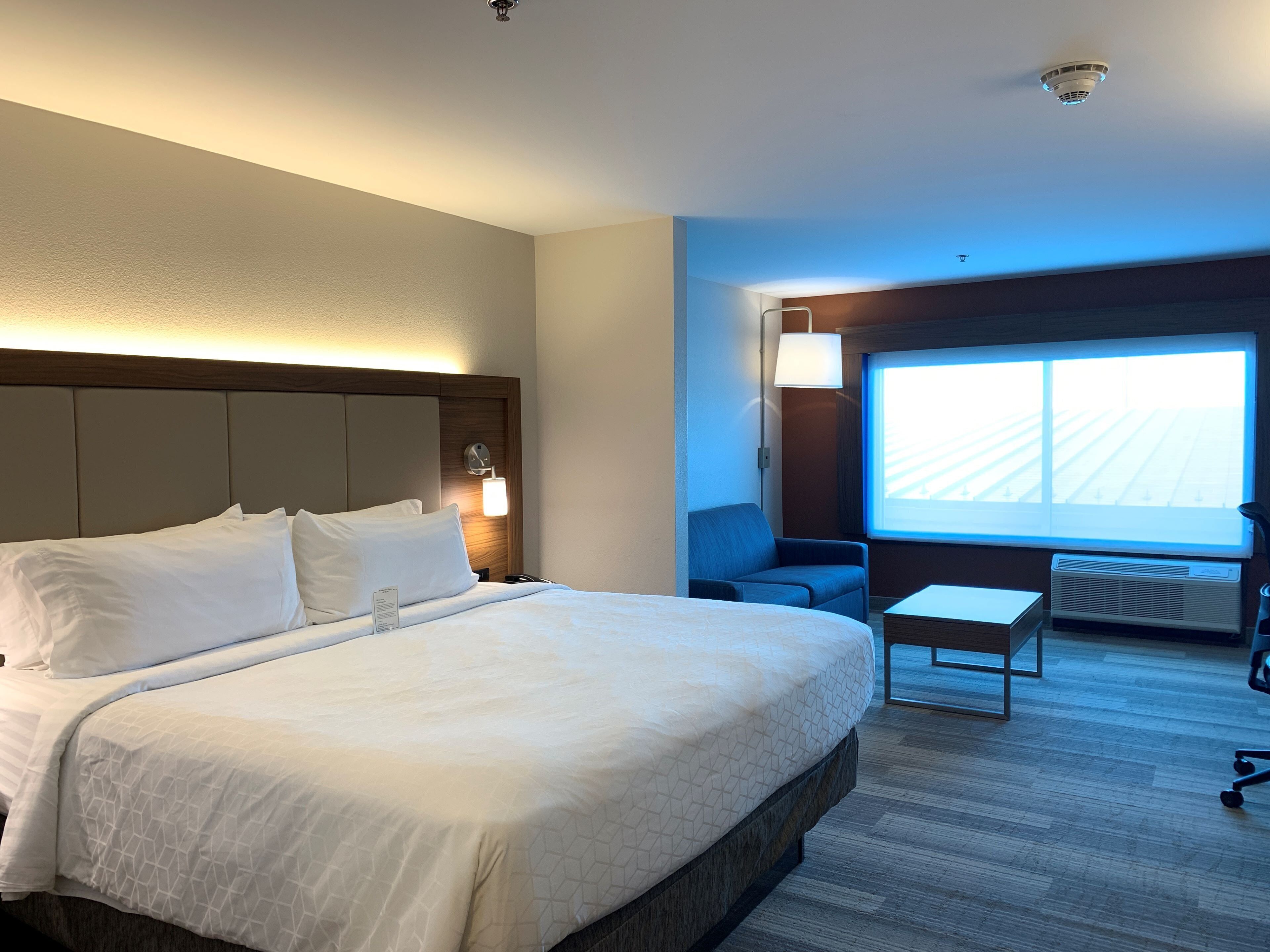 Habitación de hotel con una cama grande, un escritorio, una silla y una ventana que ofrece vistas a un edificio.