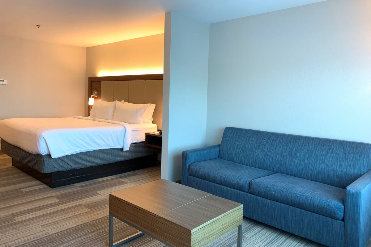 A hotel room with a bed, a blue sofa, and a wooden coffee table.