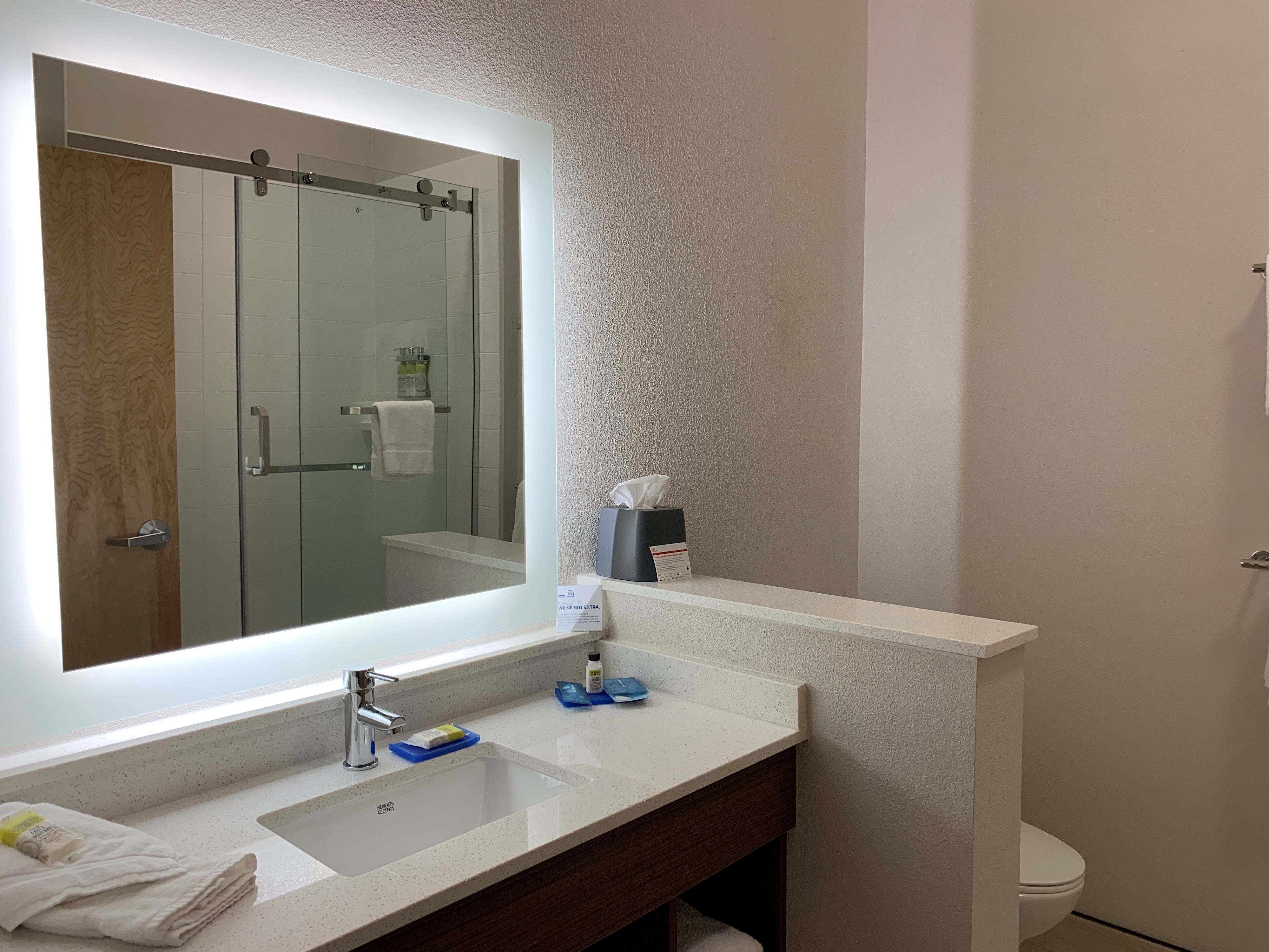 A bathroom with a large mirror, a sink, a toilet, and a shower area.