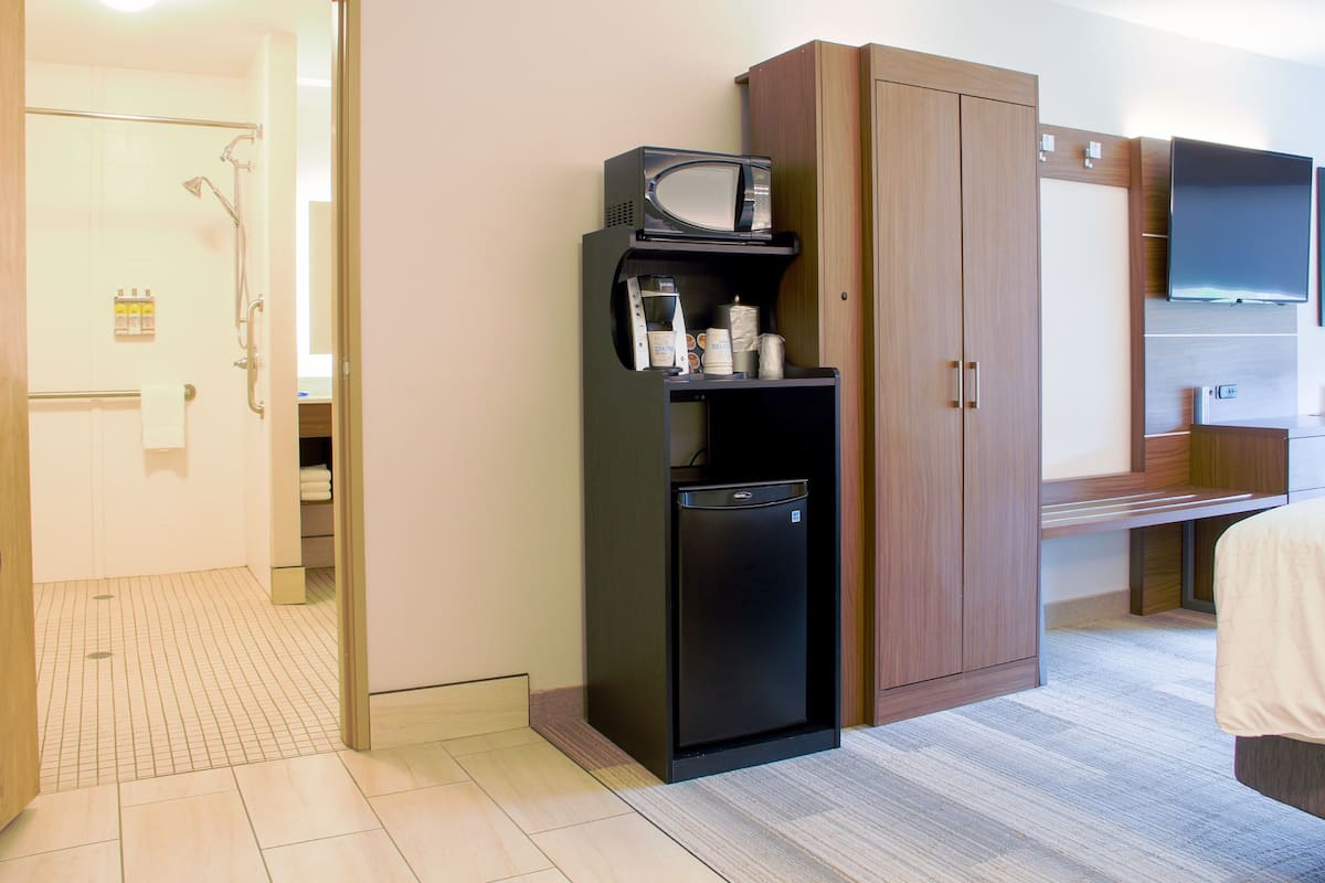 A hotel room with a kitchenette, a microwave, a refrigerator, and a television.
