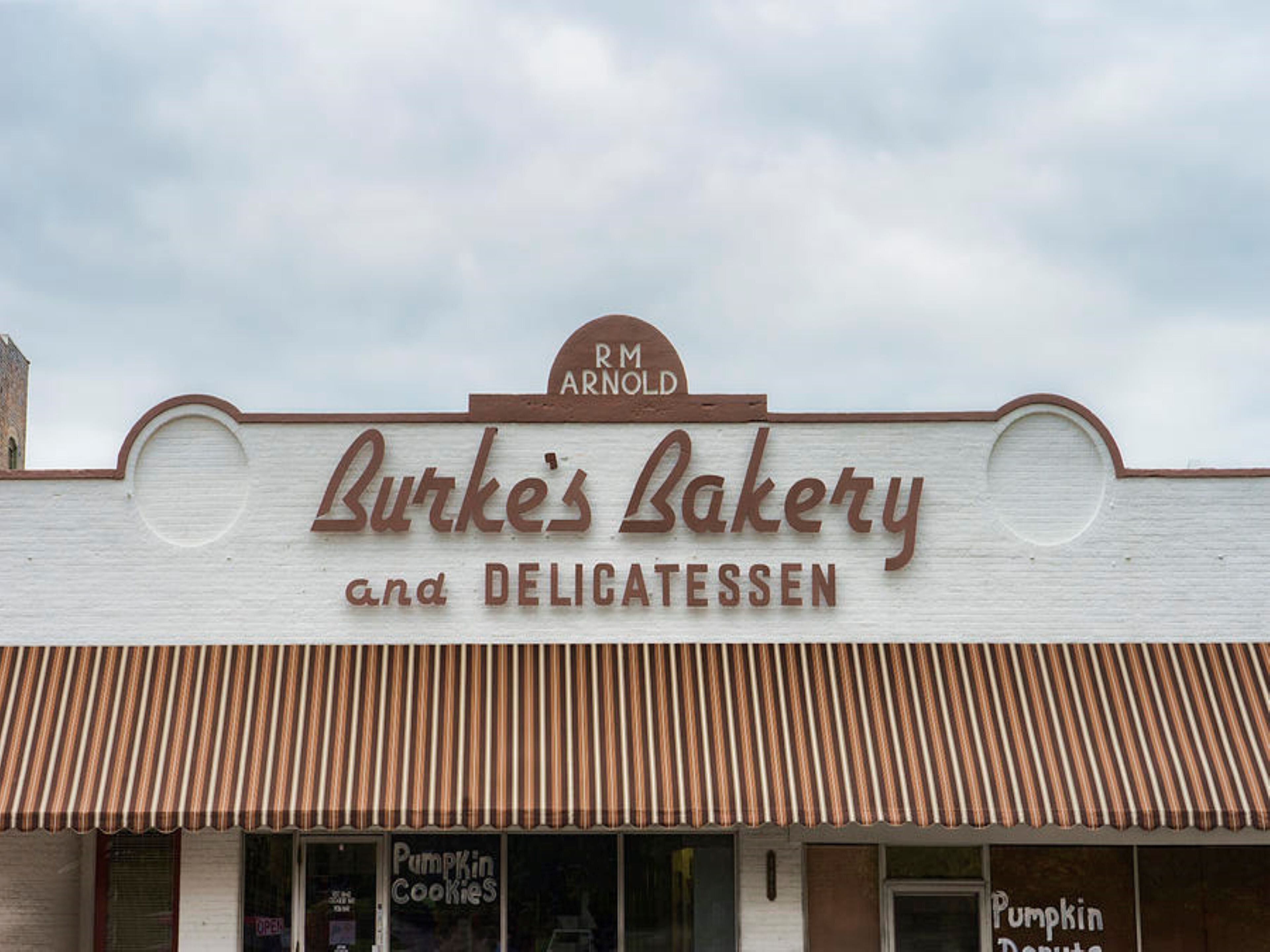 A storefront with a sign for 'Burke's Bakery and Delicatessen' and a 'Pumpkin Cookies' window display.