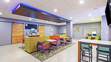A modern hotel lobby with a reception desk, seating area, and a large screen.