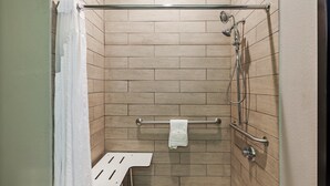 A walk-in shower with a glass door, a white bench, and a towel rack. - Holiday Inn Express & Suites Perryton by IHG (Perryton)