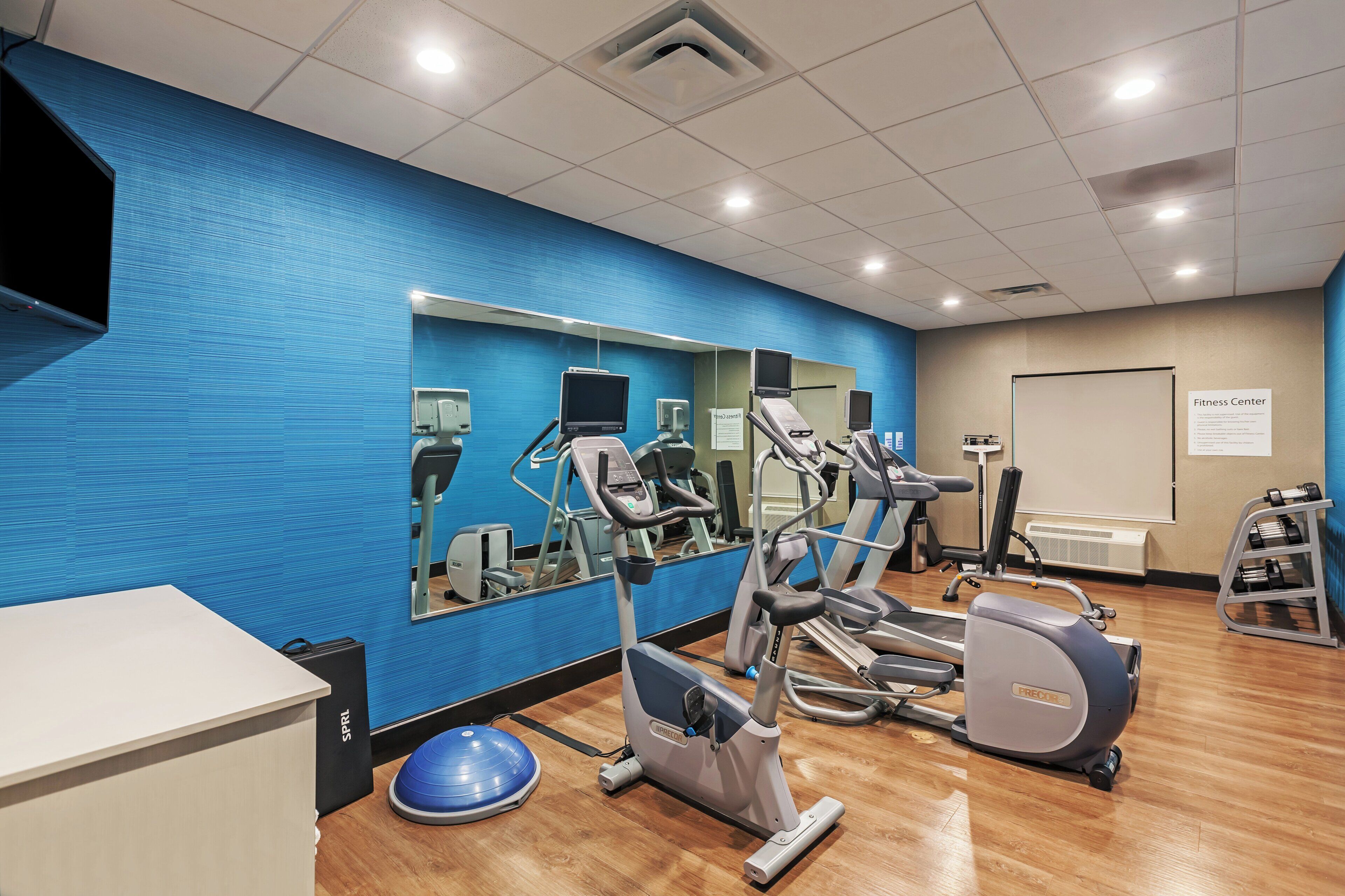 A fitness center with exercise equipment, a mirrored wall, and a whiteboard with a sign.