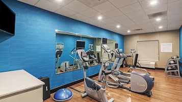 A fitness center with exercise equipment, a mirrored wall, and a whiteboard with a sign.