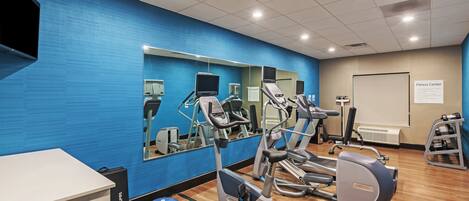 Une salle de sport équipée de matériel d’exercice, dotée d’un mur miroir et d’un tableau blanc sur lequel est affiché un panneau.