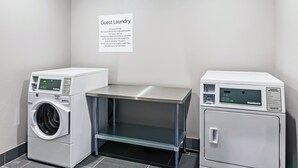 A guest laundry area with two washing machines and a table, a sign with laundry instructions, and a tiled floor. - Holiday Inn Express & Suites Perryton by IHG (Perryton)