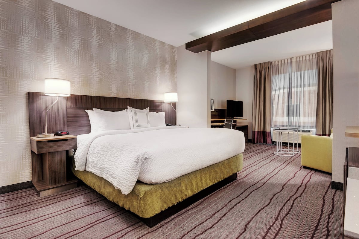 A hotel room with a large bed, two bedside lamps, a TV, a desk, and a chair.