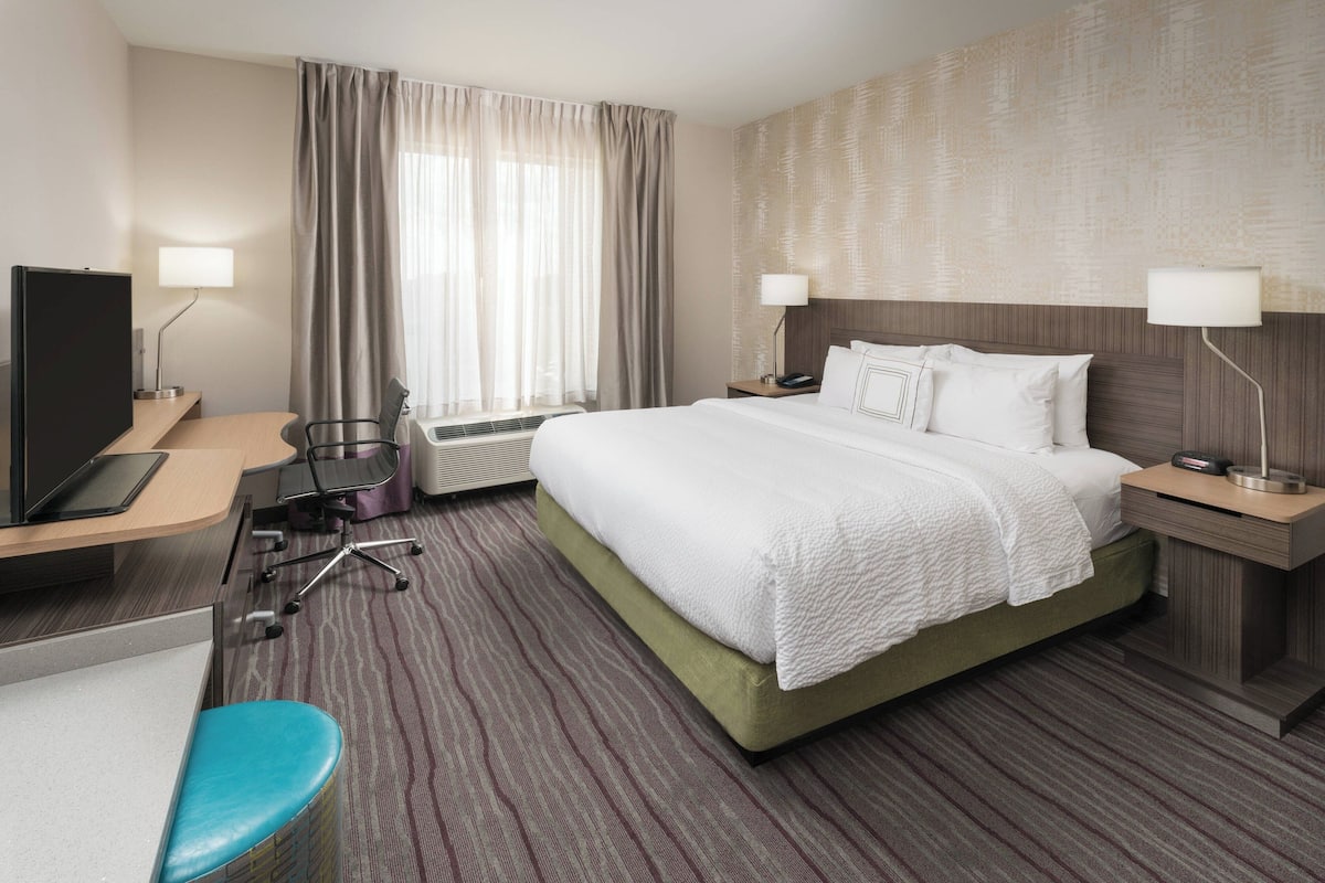 A hotel room with a bed, a desk, a chair, a television, and a window with curtains.