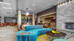 A modern lobby with a blue sectional sofa, a round wooden table, and a patterned carpet. - Fairfield Inn & Suites by Marriott Chicago Schaumburg (Schaumburg)