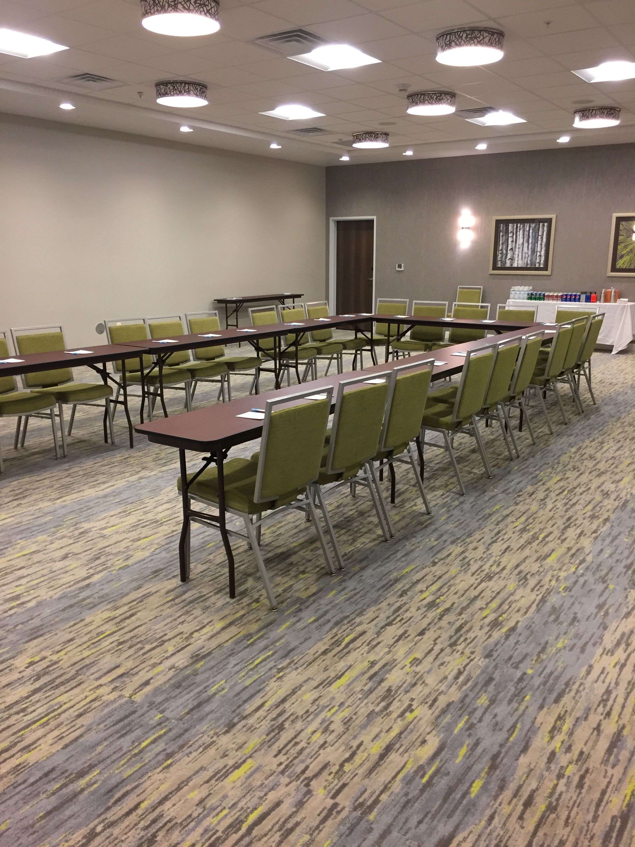 A conference room with long tables and green chairs, carpeted floor, and ceiling lights.