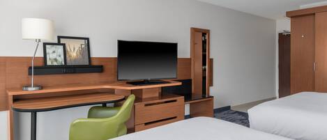 A hotel room with a bed, a desk with a chair, a television, and a wardrobe.