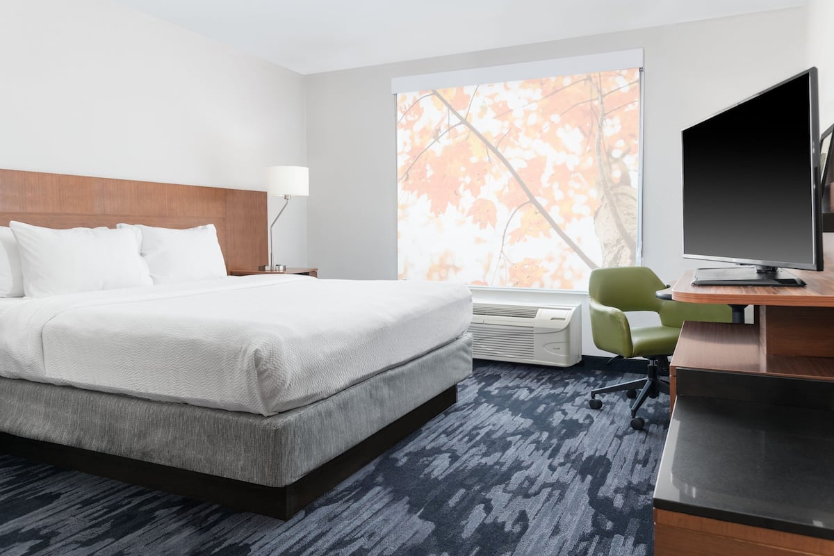 Une chambre d’hôtel avec un grand lit, un bureau avec un ordinateur, une chaise et une fenêtre donnant sur des arbres.