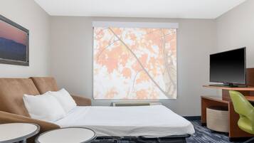 Habitación de hotel con cama, sofá, televisor, escritorio y ventana con hojas otoñales.