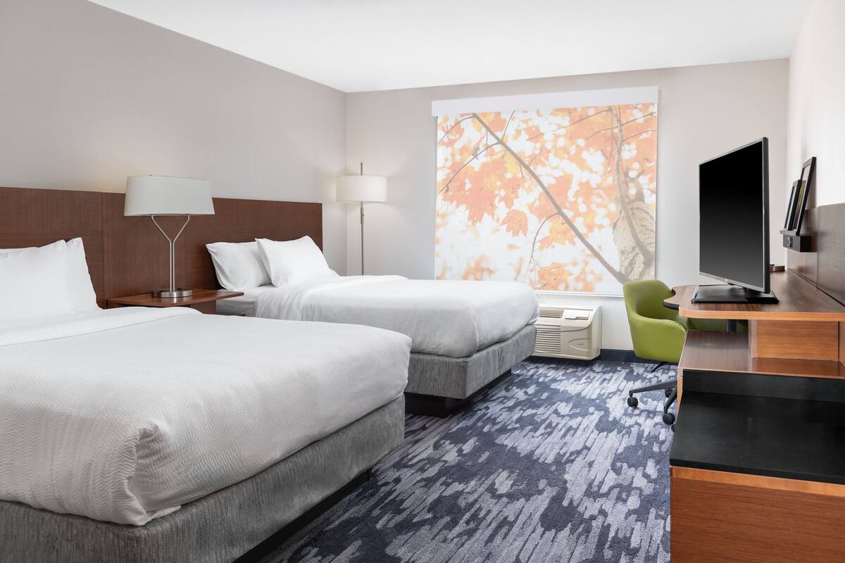 Une chambre d’hôtel avec deux lits, un bureau, une télévision et une grande fenêtre donnant sur un arbre.
