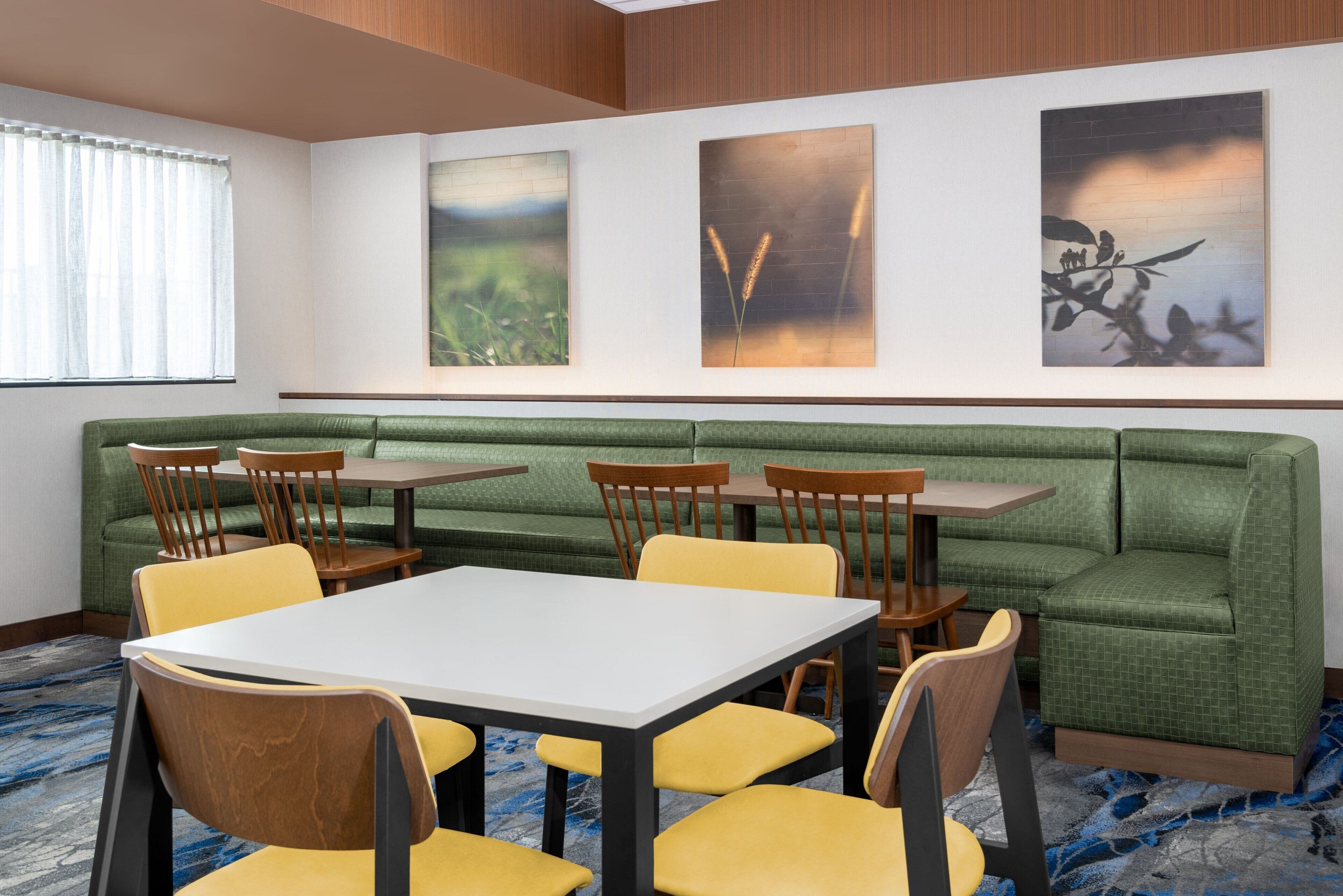 A conference room with a green sofa, yellow chairs, and a white table. There are three paintings on the wall.