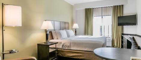 A hotel room with a bed, two bedside lamps, a TV mounted on the wall, a desk, and a chair.