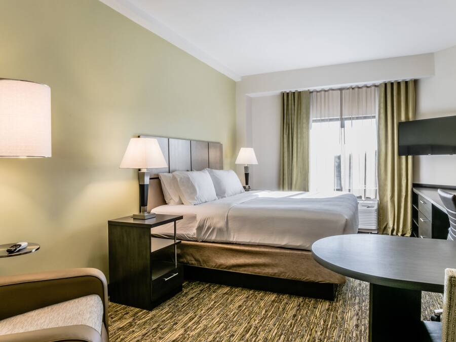 A hotel room with a bed, two bedside lamps, a TV mounted on the wall, a desk, and a chair.
