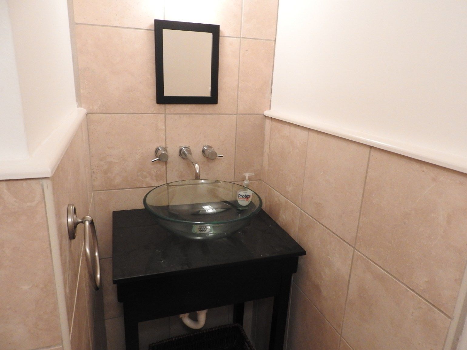 Un baño con un lavabo de cristal, un tocador negro y un espejo en la pared.