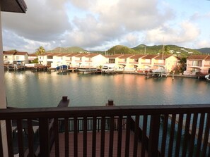 A marina with docked boats and a row of houses with balconies, overlooking a calm body of water and hills in the background. - Villa 230C at Jolly Harbour (Jolly Harbour)