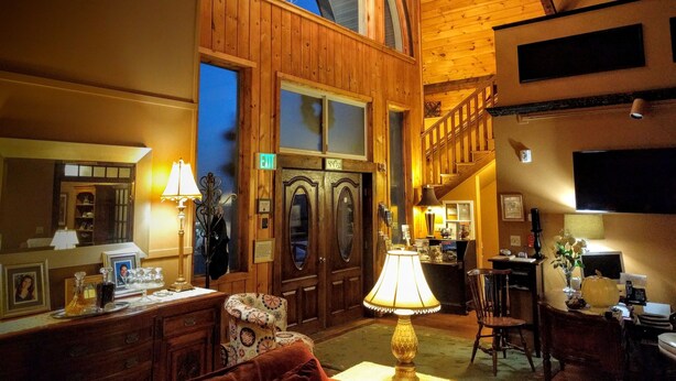A spacious lobby with a high ceiling, wooden walls, and a chandelier. There is a reception desk, a staircase, and a dining area with chairs and a table. - Haven By The Sea B&B Inn (Wells)
