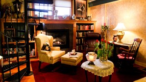 A cozy living room with a fireplace, bookshelves, a comfortable armchair, and a small table with a vase of flowers. - Haven By The Sea B&B Inn (Wells)