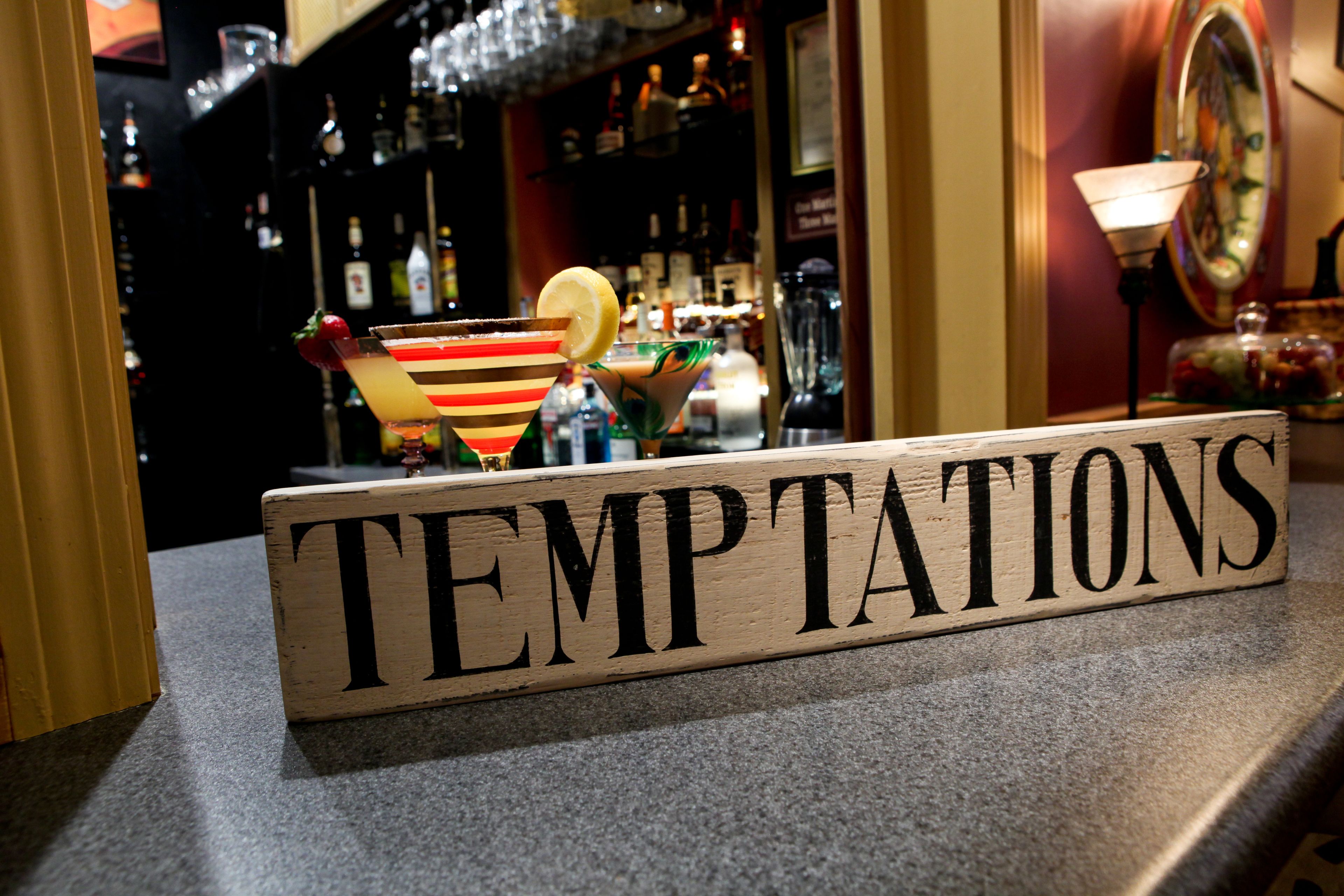 Una barra con un letrero que dice "TEMPTATIONS" y varios vasos de cóctel.
