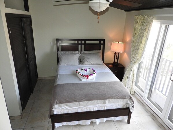 Una cama bien tendida con edredón blanco y gris, un cabecero de madera y una mesita de noche con una lámpara.