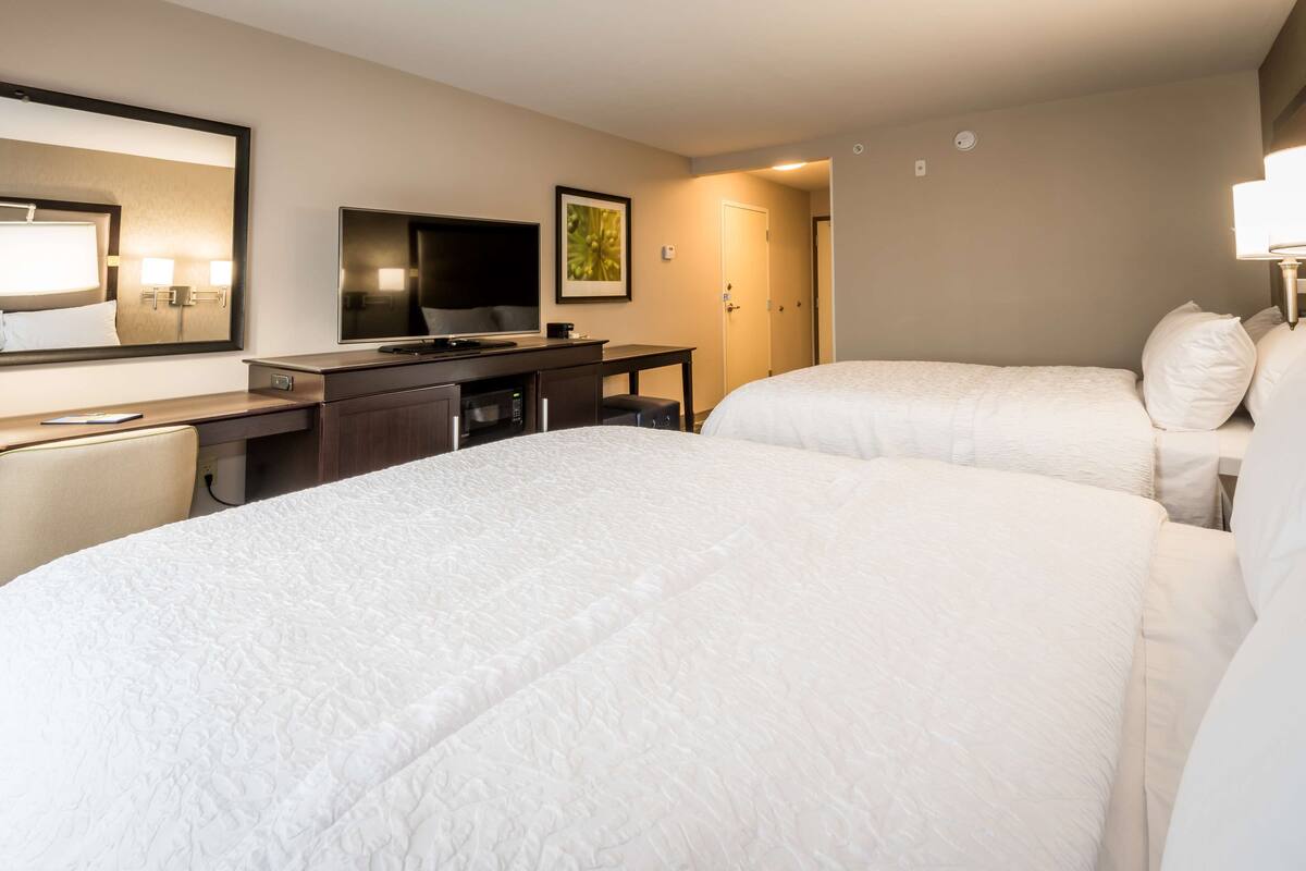 A hotel room with two beds, a desk with a television, and a mirror.