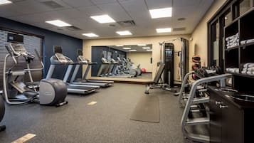Une salle de sport équipée de tapis de course, de vélos elliptiques, d’un banc de musculation et d’un miroir.