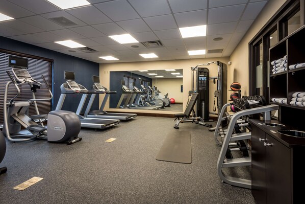 Une salle de sport équipée de tapis de course, de vélos elliptiques, d’un banc de musculation et d’un miroir.
