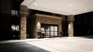A hotel entrance with a stone facade, large glass doors, and a red carpet leading to the entrance.
