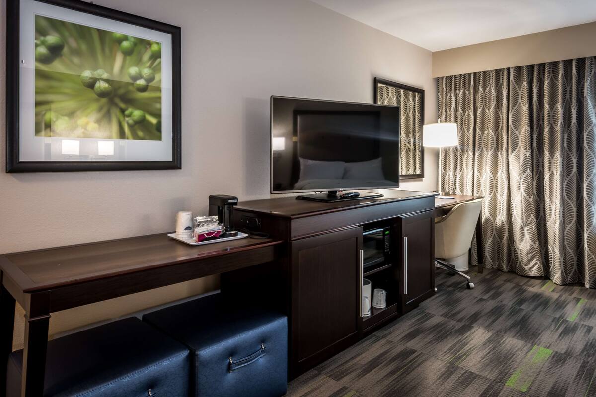 A hotel room with a desk, television, and a minibar.