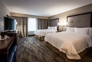 Habitación de hotel con dos camas, un escritorio, televisor y ventana con cortinas.