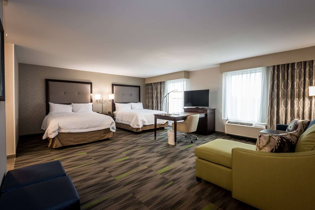 A hotel room with two beds, a desk, a television, and a sofa.