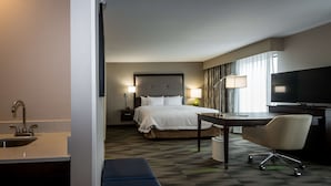 A hotel room with a bed, bedside table, lamp, desk, chair, TV, and a sink.