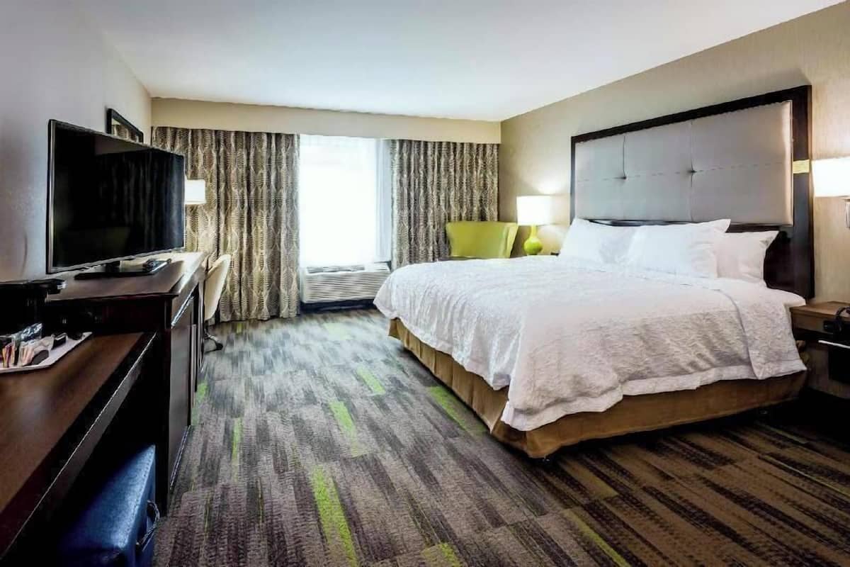 A hotel room with a bed, a desk with a television, a chair, and a window with curtains.
