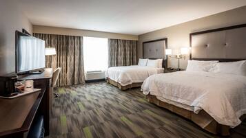 A hotel room with two beds, a desk with a computer, a TV, and a large window with curtains.