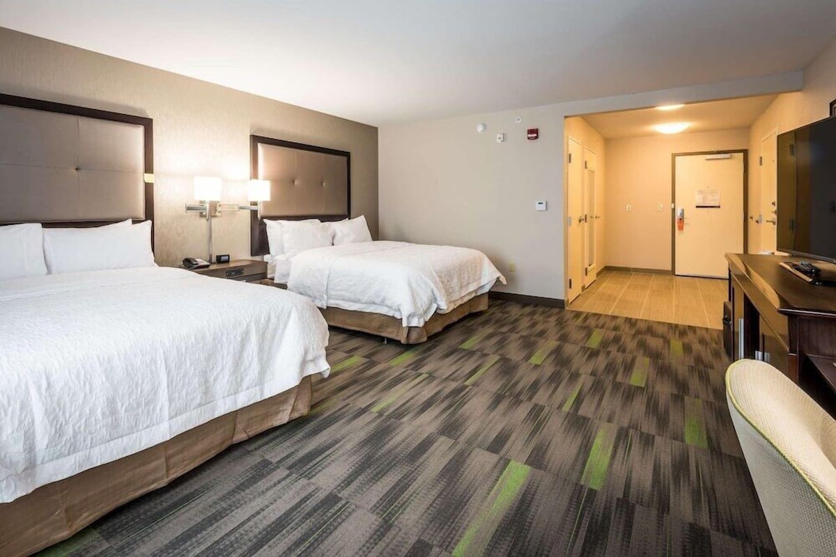 A hotel room with two beds, a desk, a chair, and a television.