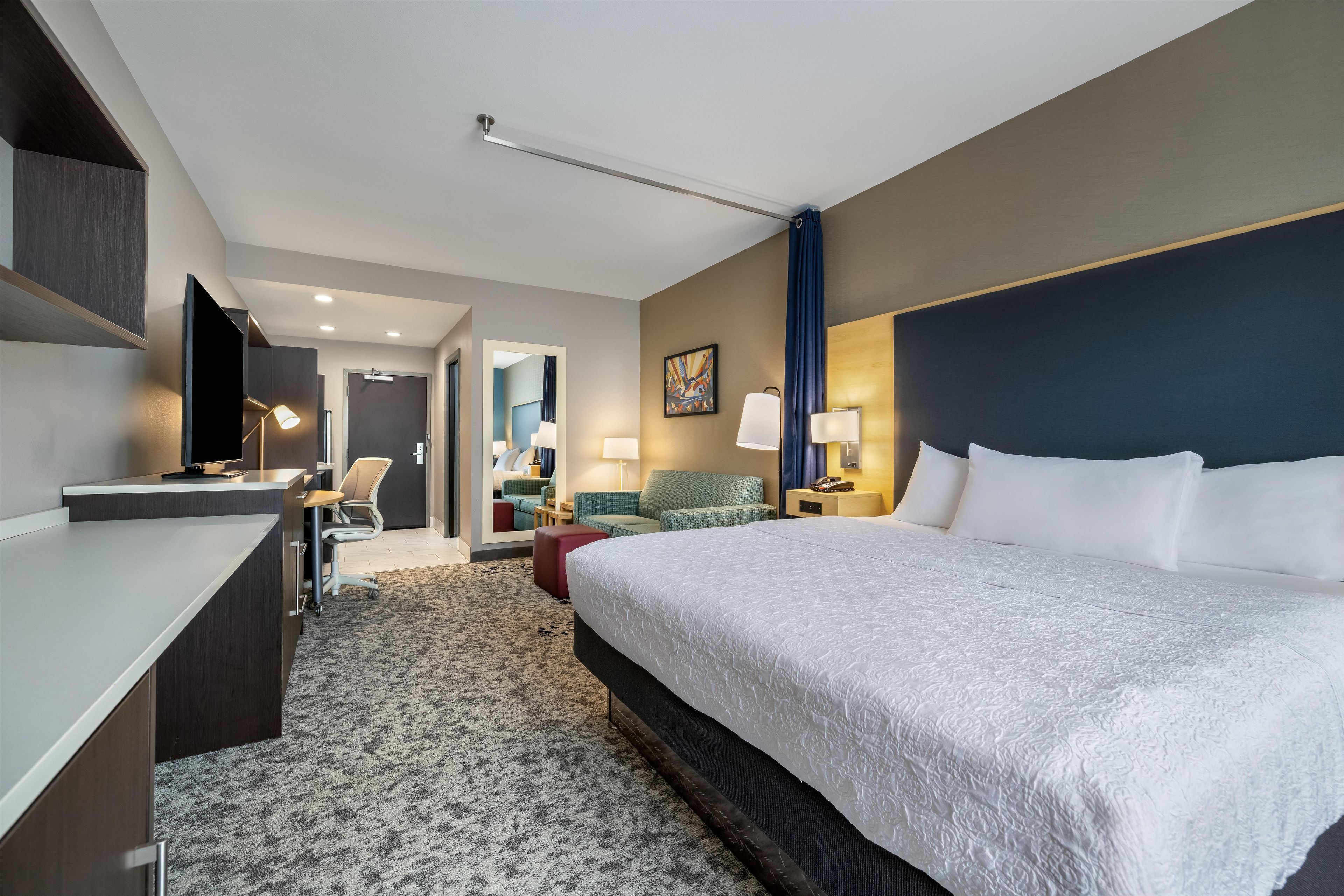 A hotel room with a large bed, a desk, a chair, a sofa, and a TV.